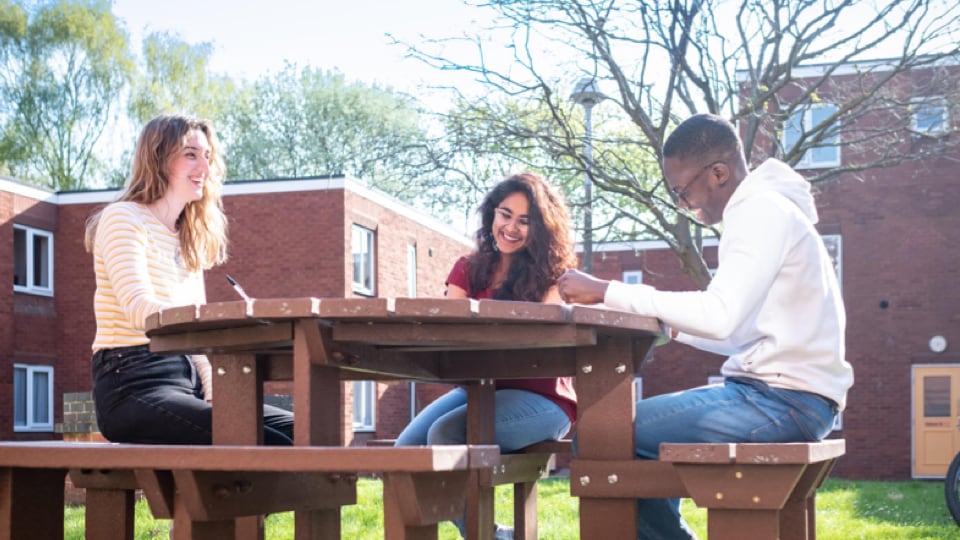 Three students sitting together outside at a table bench